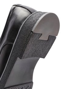Zwarte leren schoen met een gestructureerde rubberen zool, featuring een gladde bovenkant en een iets verhoogde hak. De zool heeft een patronen ontwerp.