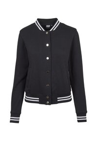 Veste varsity noire avec des bandes blanches sur le col, les poignets et la taille, boutons-pression sur le devant et deux poches latérales.