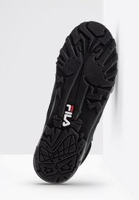 Suola di sneaker nera in gomma con scanalature profonde, dotata di un logo "Fila" bianco e rosso. I modelli testurizzati migliorano la presa e la durabilità.