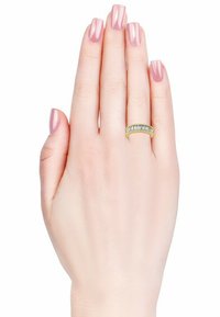 Anello in oro con una fila di piccole pietre trasparenti. Mano con smalto rosa chiaro mostra l'anello su uno sfondo bianco semplice.
