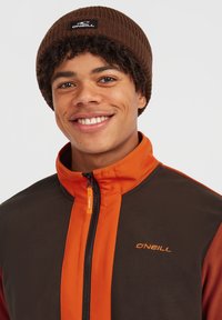 Fleecejakke med brune og orange paneler, frontlynlås og O'Neill-logo. Parret med en brun ribbet hue.