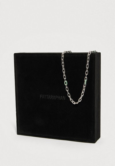Srebrny łańcuszek z zielonymi kamieniami, ułożony na czarnym welwetowym pudełku z tłoczonym napisem "PATTARAPHAN".