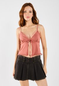 Rosa cami med volanger og frontknute, kombinert med et svart denimskjørt med folder og frynset kant.