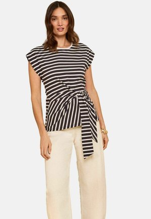 Kvinde iført sort-hvidt top med korte ærmer og vandrette striber, bundet i taljen, kombineret med beige, højttaljede bukser med vide ben.