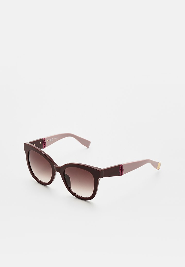 Lunettes de soleil style œil de chat avec des montures bordeaux foncé, des verres dégradés et des branches bordeaux clair ornées d'un accent doré et d'un détail de logo.
