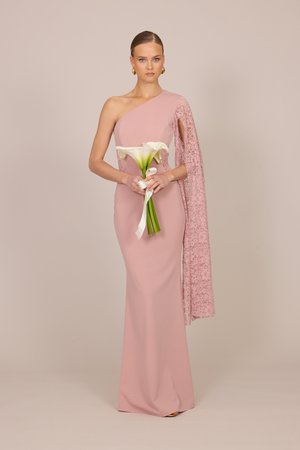 Femme en robe rose pâle à une épaule avec drapé en dentelle tenant un bouquet de callas blancs lié par un ruban blanc sur un fond neutre.
