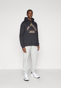 Juodas džemperis su "Los Angeles Lakers" tekstu geltonai ir purpurinai, derinamas su šviesiai pilkomis sportinėmis kelnėmis ir baltomis sportinėmis bateliais. Lygus audinio paviršius.