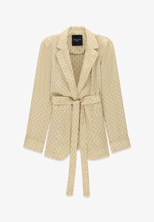 Beżowa marynarka z białym wzorem "M" na całej powierzchni, długimi rękawami, wyciętym kołnierzem, przednimi naszywanymi kieszeniami i paskiem w talii do samodzielnego wiązania.