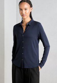 Marineblauwe overhemd met lange mouwen, voorzien van een knoopsluiting, knopen aan de voorkant en een zachte, gladde textuur. Gecombineerd met losse zwarte broek.