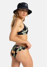 Black bikini with floral patterns in green and orange, featuring a triangle top and matching briefs. Worn with a black bucket hat.