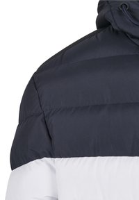 Pūķa jaka ar tumši zilu augšdaļu un baltu apakšdaļu. Piedāvā kapuci, quilted rakstu un ūdensizturīgu audumu.