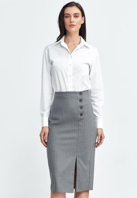 Biała koszula z długim rękawem połączona z szaro-paskowaną spódnicą ołówkową z przodu z guzikami i rozporkiem po bokach.