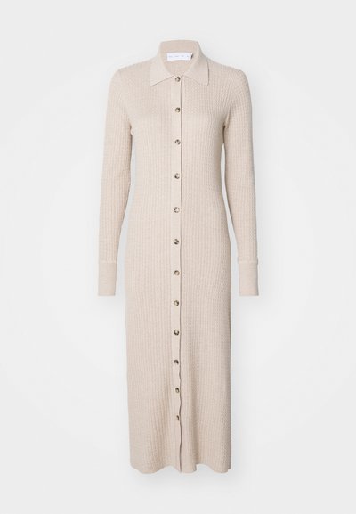 Šviesiai rudas raukinis megztinis su apykakle, ilgomis rankovėmis, mygtukų uždarymu priekyje ir prigludusia siluetu. Pasiekia po keliu, su raukinėmis rankovėmis.