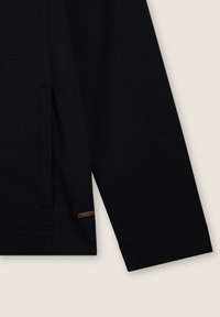 Felpa nera con un design testurizzato, tasca laterale e un sottile accento metallico. Tessuto morbido con orlo e dettagli dei polsini puliti.