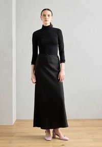 Haut col roulé noir à manches longues associé à une longue jupe maxi noire fluide. Chaussures à talons blocs rose clair avec un bout arrondi.