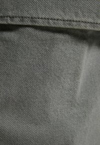 Zelená deninová látka s texturedním povrchem, která má jemný vzor tkaní a rovný střih. Materiál je pevný a hladký.