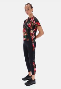Czarny kwiatowy crop top z różowymi i zielonymi wzorami zestawiony z czarnymi legginsami z kwiatowymi bocznymi panelami. Całość dopełniają czarne buty sportowe.