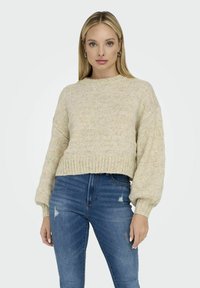 Pull en crème tricoté avec un motif texturé, encolure ronde et coupe décontractée. Associé à un jean bleu taille haute avec des détails déchirés.