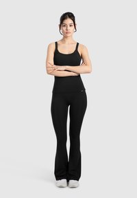 Top atletico nero con spalline sottili e design aderente, abbinato a leggings neri a zampa e scarpe da ginnastica bianche.