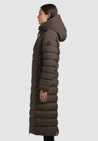 Cappotto invernale lungo e imbottito di colore marrone scuro con cappuccio, design trapuntato orizzontale, chiusura frontale con cerniera e tasche laterali. Materiale liscio e resistente all'acqua.