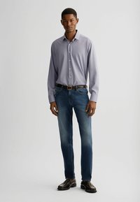 Camicia a maniche lunghe a righe viola chiaro con pattina a bottoni, abbinata a jeans diritti blu sbiaditi e scarpe in pelle scura.
