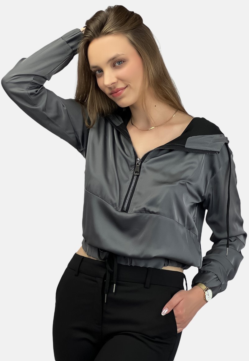 Szara kurtka w kroju do pasa z zamkiem z przodu, kapturem i czarnymi akcentami. Posiada gładki, błyszczący materiał oraz regulowany sznurek w talii. Czarne spodnie.