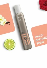 Wella Shape Control spray i en cylindrisk, mat taupe beholder med et hvidt låg. Har et logo og tekst i orange. Inkluderer lime- og blomsterakcenter.