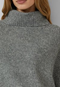 Grijze gebreide coltrui met geribbelde textuur; losse pasvorm; zacht materiaal; voorzien van een hoge kraag met gelijkmatige stiksels.