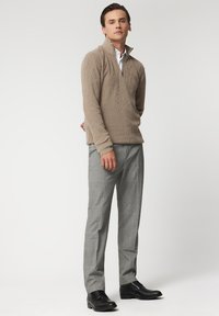 Beżowy sweter z dzianiny z pół-zamkiem, zestawiony z jasnoszarymi spodniami w kratę i czarnymi sznurowanymi butami, charakteryzujący się gładką teksturą i dopasowanym krojem.