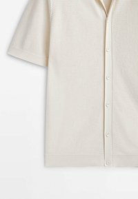 Cardigan en maille à manches courtes de couleur crème avec un motif texturé, fermeture boutonnée à l'avant et bords côtelés aux manches et à l'ourlet.