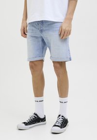 Ljusblå denimshorts med upprullade fållar, bärs med svarta sneakers och vita ankelsockor med svart text. Enkel design, avslappnad passform.
