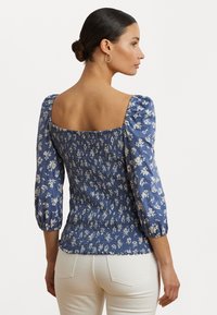 Blaue Bluse mit floralem Muster, quadratischem Ausschnitt, gepufften Ärmeln und gerafften Details. Stoff: leicht. Akzente am Saum: gerafft.