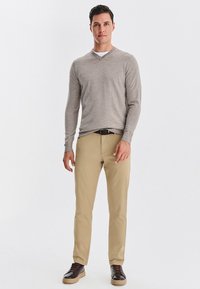 Jasnoszara sweter z dekoltem w serek, beżowe spodnie i ciemne sportowe buty. Sweter ma gładką teksturę; spodnie prostą nogawkę o luźniejszym kroju.