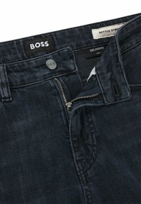 Mörkblå slim-fit denimjeans med dragkedja i metall, knappstängning och varumärkesetikett "BOSS" på midjan. Texturen är slät och hållbar.