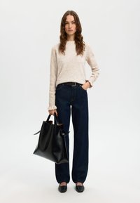 Maglione a maglia beige, jeans a gamba larga blu scuro, borsa tote in pelle nera con due manici e scarpe slip-on nere. Materiali testurizzati in tutto.