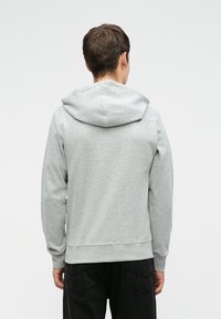 Sweatshirt gri cu glugă, fabricat dintr-un material moale, având o buzunar tip cangur și manșete țesute. Design simplu, fără modele vizibile.