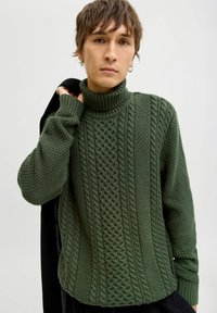 Pull en maille vert foncé avec un col roulé, présentant un motif de câble texturé et des poignets côtes. Tissu doux et épais, coupe décontractée.