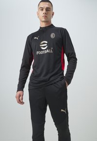 Black athletic tracksuit with a half-zip collar and red side panels. Features gold logo and brand accents on the shirt and pants.