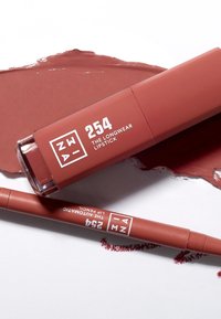 Langvarig leppestift og matchende leppeblyant i en matt, dempet rød nyanse. Begge tubene har hvit trykt tekst og et stilrent design.