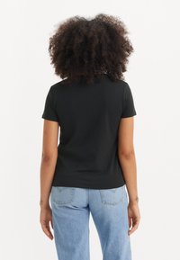 T-shirt noir à manches courtes en coton doux, avec un col rond classique et une coupe décontractée, assorti à un jean en denim bleu clair.