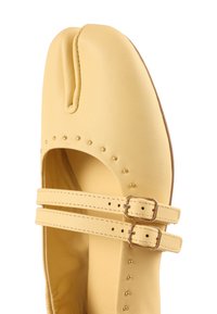 Ballerine en cuir jaune à bout fendu avec deux brides à boucle et petits clous dorés le long des bords.