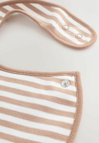 Tissu rayé beige et blanc avec bords arrondis et boutons-pression, probablement une partie d'un bavoir pour bébé ou d'un accessoire vestimentaire similaire.