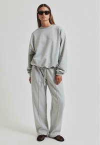 Sudadera de algodón gris con hombros caídos, combinada con pantalones de chándal grises a juego que cuentan con una cinturilla con cordón y zapatos slip-on de malla negra.