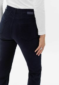 Donkerblauwe corduroy broek met een getailleerde pasvorm, achterzakken en een gestructureerd oppervlak, gecombineerd met een wit shirt met lange mouwen.