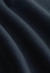 Donker marineblauwe stof met een gladde textuur, met zachte plooien en een fijn breipatroon, waardoor de diepte en de structuurdimensies worden benadrukt.