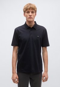 Fekete galléros póló rövid ujjakkal és háromgombos gombolattal. A bal mellrészen kör alakú logó díszíti.