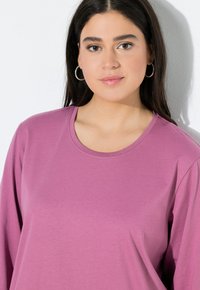 T-shirt a maniche lunghe in morbido tessuto rosa, con scollo rotondo e una texture liscia. Vestibilità morbida con dettagli di cucitura minimi.