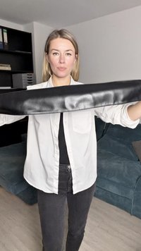 Crni kožni pojas s glatkom teksturom, držan horizontalno. Ima minimalistički dizajn i širok je s šivenim rubovima.