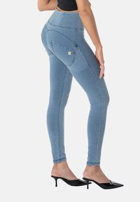 Leggings de mezclilla azul de talle alto con textura suave, que presentan bolsillos traseros curvos y costuras contrastantes, combinados con mules negros de tacón.