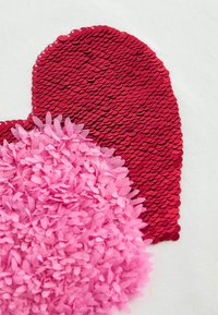 Red sequined heart shape and pink fabric with raised floral texture, both against a white background.